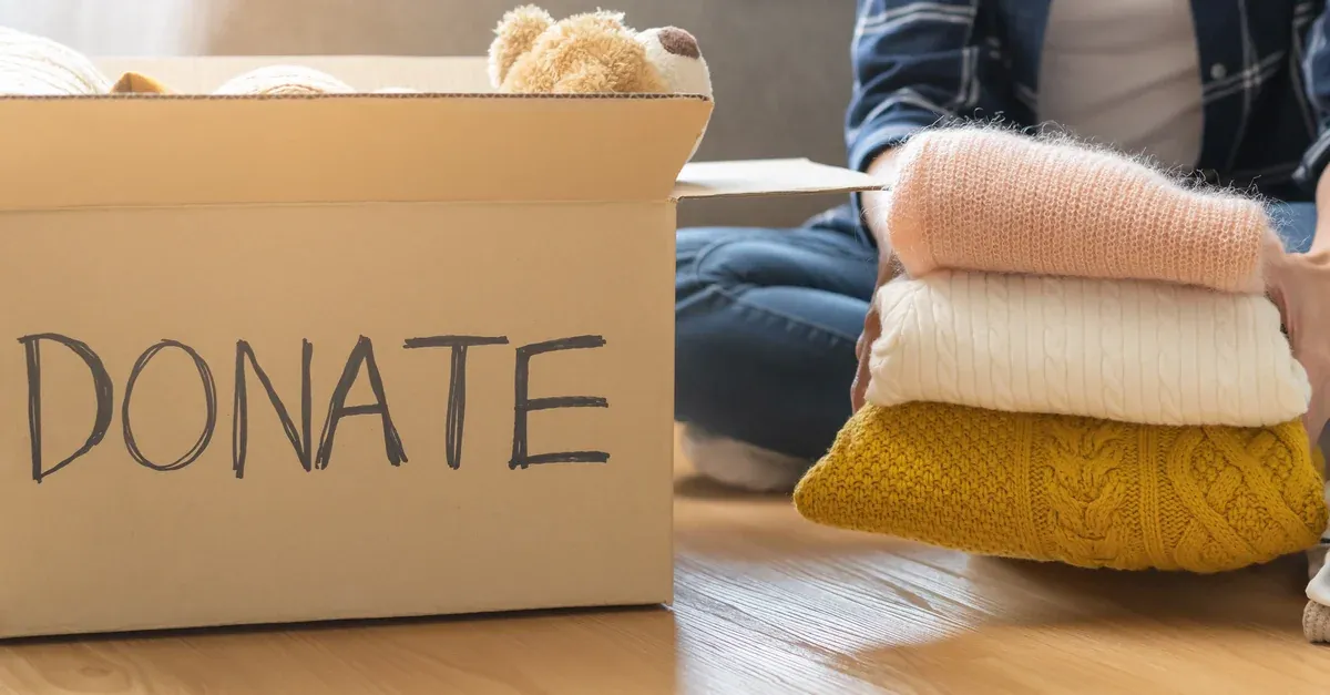 Person sorting folded jumpers next to a cardboard box labelled Donate, while clearing out before a house move