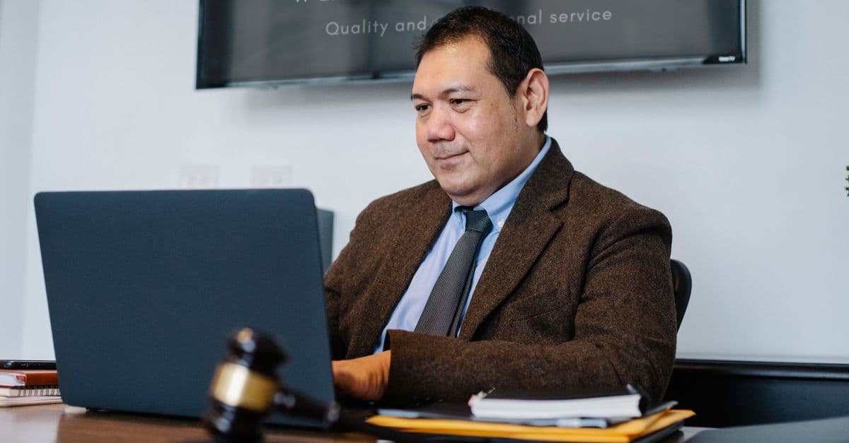 Experienced middle aged ethnic happy male working with netbook at table with judge hammer